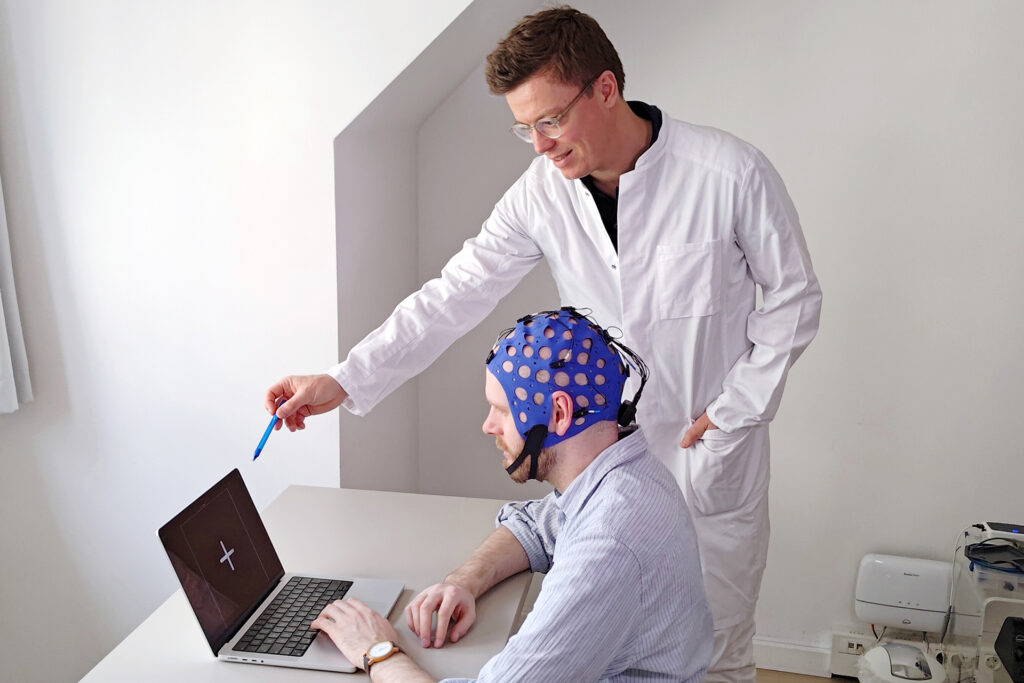 A researcher pointing at a laptop opposite to a participant wearing Mentalab's mobile EEG